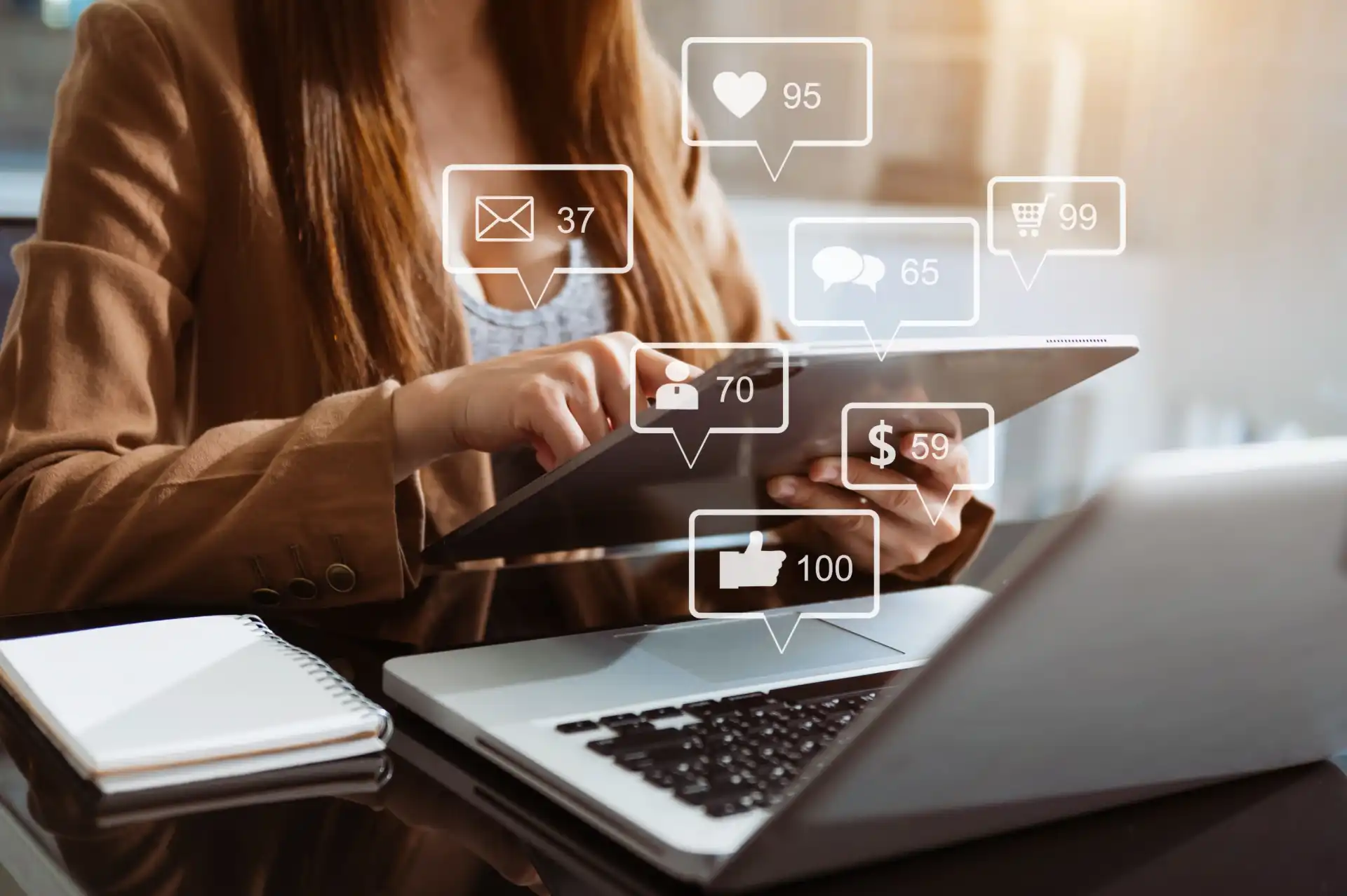 Foto de uma mulher de negócios utilizando seu laptop e tablet para checar os resultados que obteve com Social Selling para sua empresa B2B, indicados por ícones flutuantes de novos seguidores, mensagens privadas e ganhos financeiros.