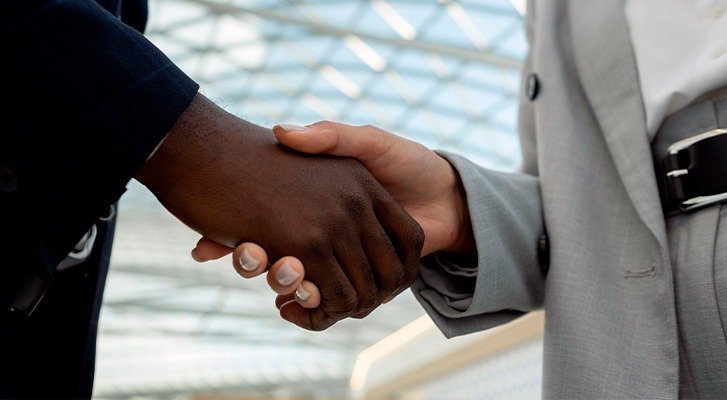 Foto de duas pessoas de gênero e etnia diferentes apertando as mãos em um cenário com iluminação natural, simbolizando a régua de relacionamento B2B.