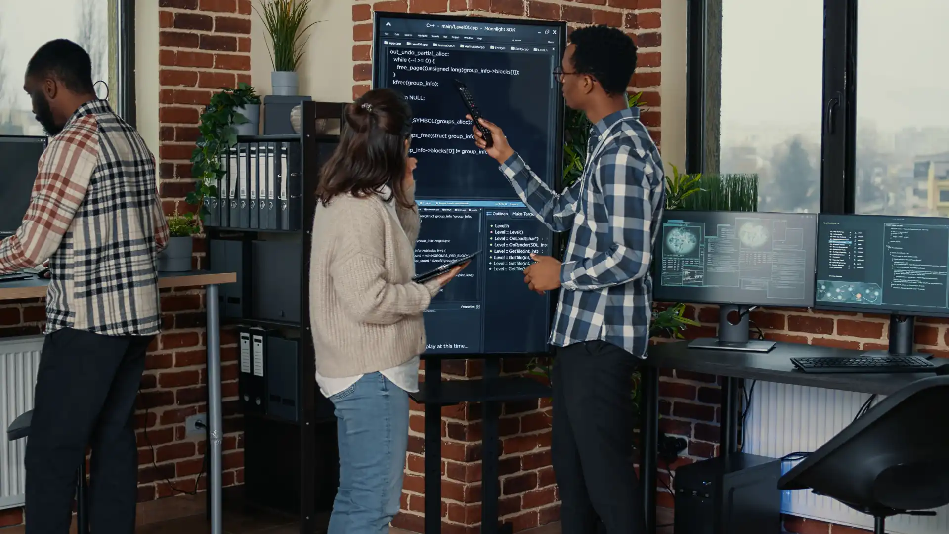 Foto de um time de desenvolvedores de uma empresa de tecnologia discutindo sobre um código em um monitor de parede.