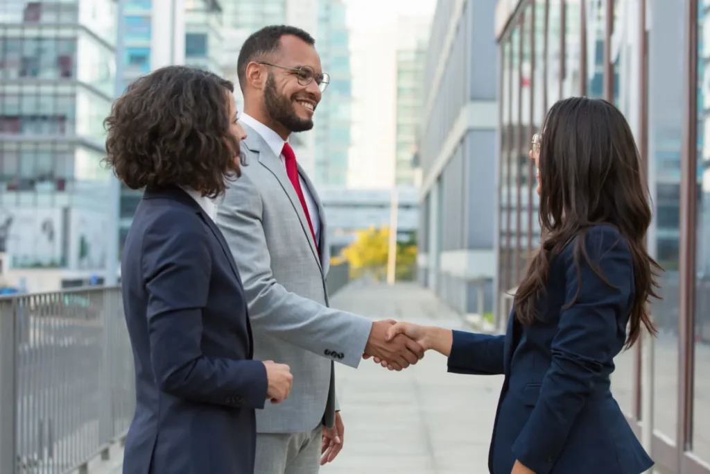 Foto de profissionais de negócios B2B em um ambiente corporativo, apertando as mãos durante uma negociação em um corredor de prédio comercial.