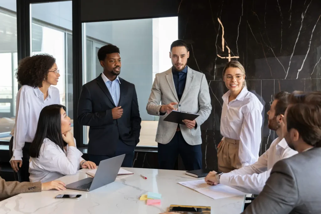 Foto de uma equipe de profissionais em reunião corporativa B2B em escritório moderno, discutindo ideias e anotando em mesa com notebooks e documentos.