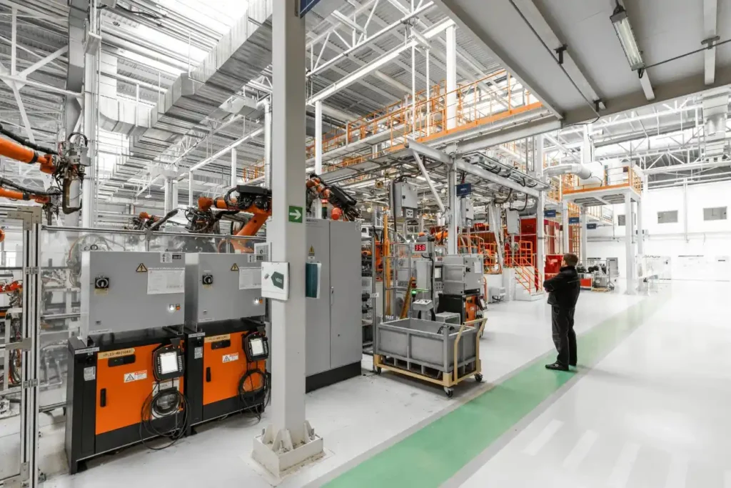 Foto da vista interna de uma planta industrial moderna com maquinários, tubulações e painéis elétricos, corredor amplo e técnico observando equipamentos em operação.