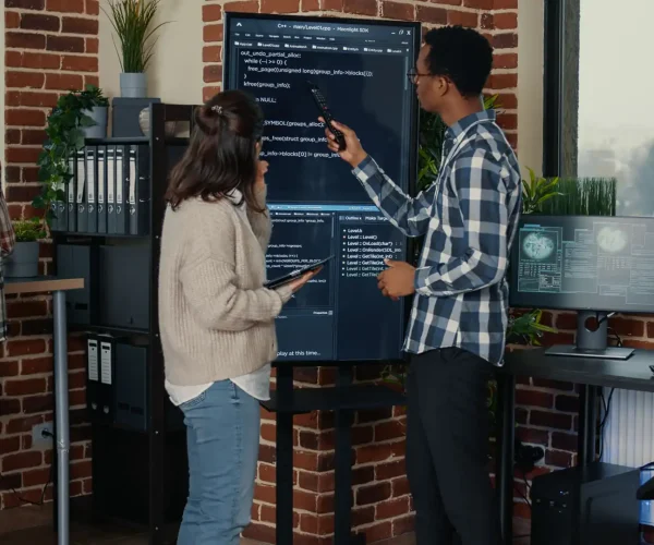 Foto de um time de desenvolvedores de uma empresa de tecnologia discutindo sobre um código em um monitor de parede.