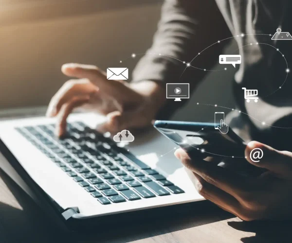 Profissional usando computador portátil e smartphone, com ícones conectados de comunicação digital, representando a abrangência do Inbound Marketing B2B.